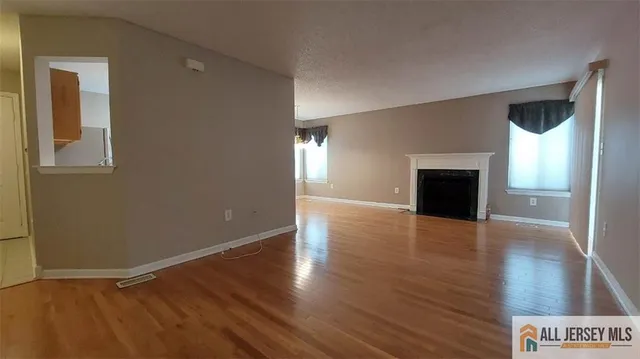 an empty room with wooden floor fireplace and windows