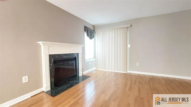 a view of an empty room with wooden floor fireplace and a window