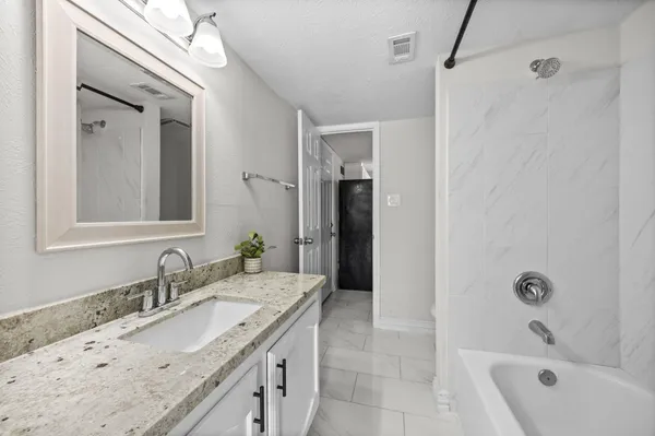 a bathroom with a granite countertop sink a mirror a bathtub and shower
