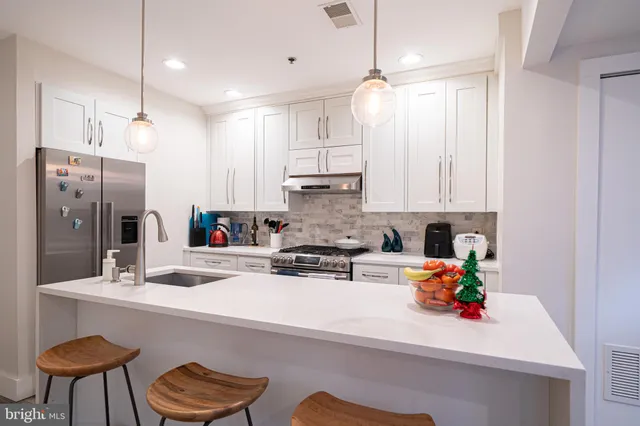 a kitchen with stainless steel appliances white cabinets a sink a stove a kitchen island with chairs and white cabinets