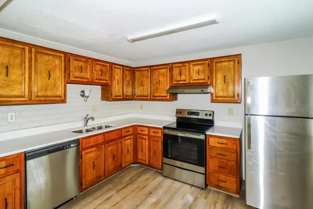 a kitchen with stainless steel appliances granite countertop a refrigerator a sink dishwasher a stove top oven and a dining table with wooden floor