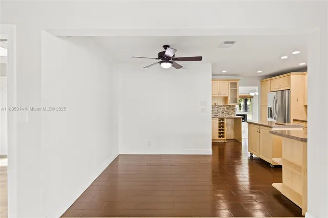 a view of an empty room and kitchen with wooden floor