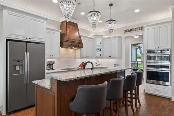 a kitchen with stainless steel appliances granite countertop a sink dishwasher a refrigerator a stove a dining table and chairs with wooden floor