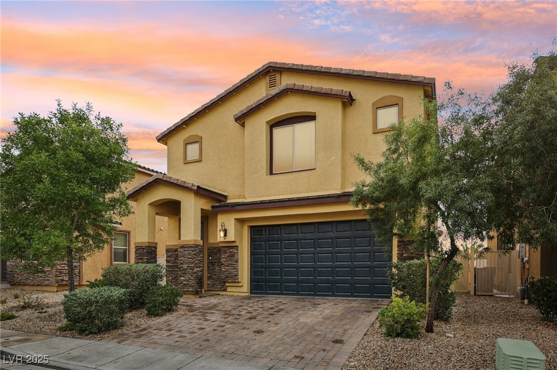 Mediterranean / spanish-style home featuring a garage, stucco siding, driveway, and stone siding