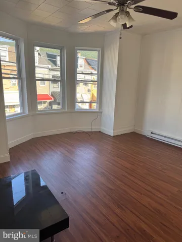 an empty room with wooden floor fan and windows
