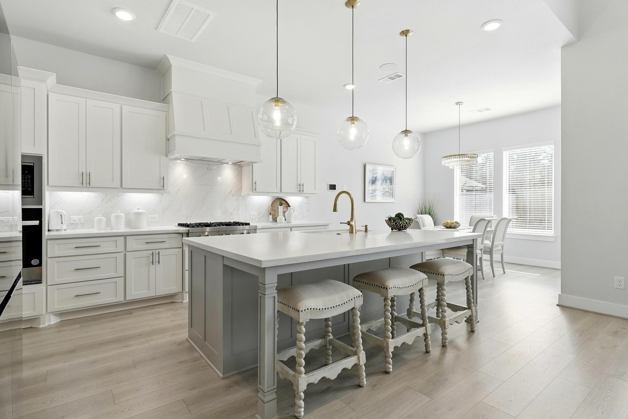 26923 Arethusa Court Spring, TX 77389 - Photo 13 of 44 This kitchen features a sleek and modern design with white cabinetry, stainless steel appliances, and a spacious island with seating. Pendant lighting adds elegance, while an adjacent dining area offers ample space for entertaining. Light wood flooring enhances the airy, contemporary feel.