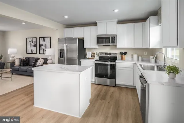 a kitchen with stainless steel appliances granite countertop a stove top oven a sink a refrigerator white cabinets and wooden floor