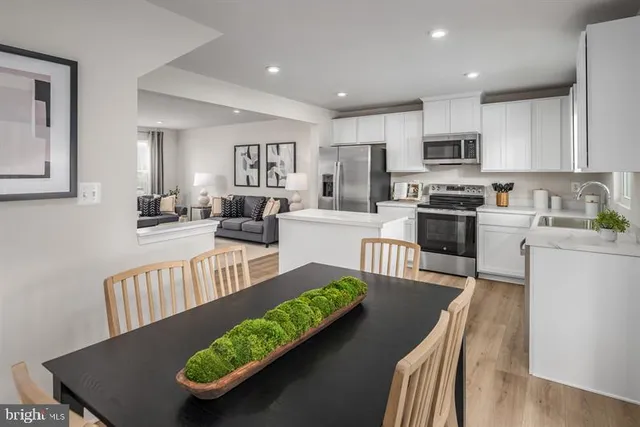 a view of a kitchen with kitchen island stainless steel appliances wooden floor dining table and chairs