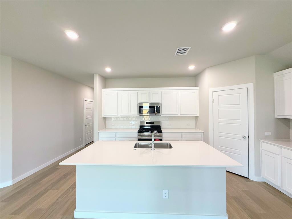 1909 Sandpiper Way Princeton, TX 75407 - Photo 5 of 35 Kitchen featuring white cabinetry, a center island with sink, stainless steel appliances, light wood-type flooring, and light stone counters