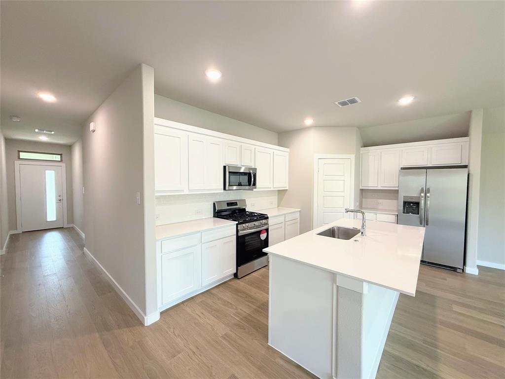 1909 Sandpiper Way Princeton, TX 75407 - Photo 6 of 35 Kitchen with stainless steel appliances, white cabinets, a center island with sink, recessed lighting, and light wood finished floors