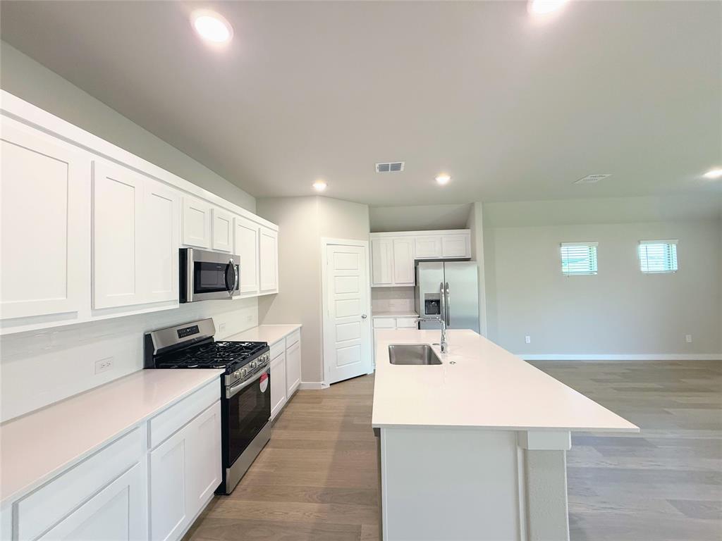 1909 Sandpiper Way Princeton, TX 75407 - Photo 7 of 35 Kitchen featuring stainless steel appliances, dark wood-style flooring, white cabinetry, recessed lighting, and an island with sink