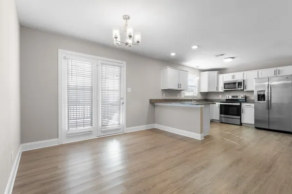 a kitchen with stainless steel appliances granite countertop a stove top oven a sink dishwasher a refrigerator and white cabinets with wooden floor