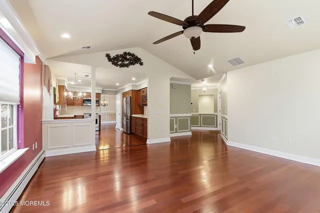 a view of an empty room with wooden floor and a kitchen