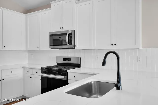 a white kitchen with stainless steel appliances granite countertop a sink a stove a microwave and cabinets