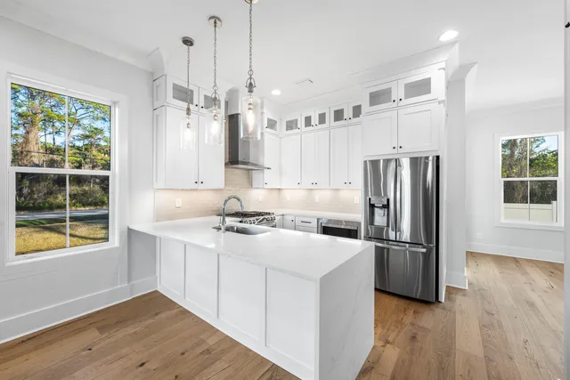 a kitchen with stainless steel appliances granite countertop a refrigerator a sink dishwasher a stove and a dining table with wooden floor