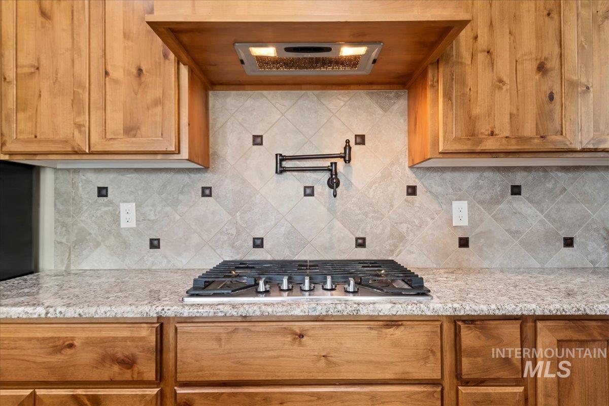 6091 East Path Drive Nampa, ID 83687 - Photo 13 of 33 Kitchen with range hood, light stone counters, tasteful backsplash, and brown cabinetry