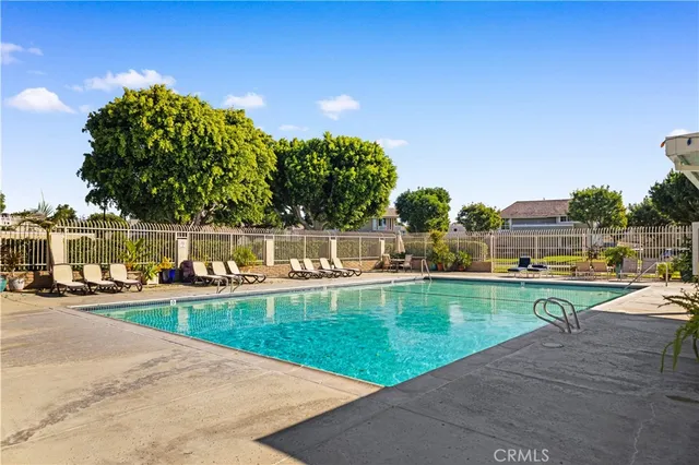 a view of a swimming pool that has lawn chairs and a dining table under an umbrella