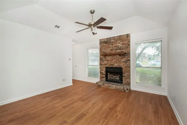an empty room with wooden floor fireplace and windows
