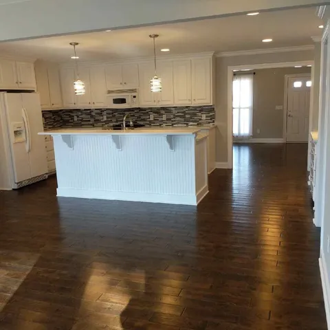 a view of a kitchen with granite countertop a stove top oven a sink and white cabinets with wooden floor