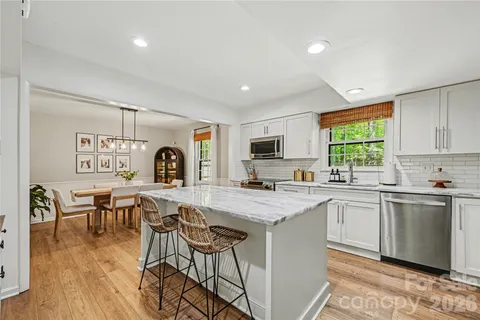 a kitchen with stainless steel appliances granite countertop a stove top oven a sink dishwasher a dining table and chairs with wooden floor