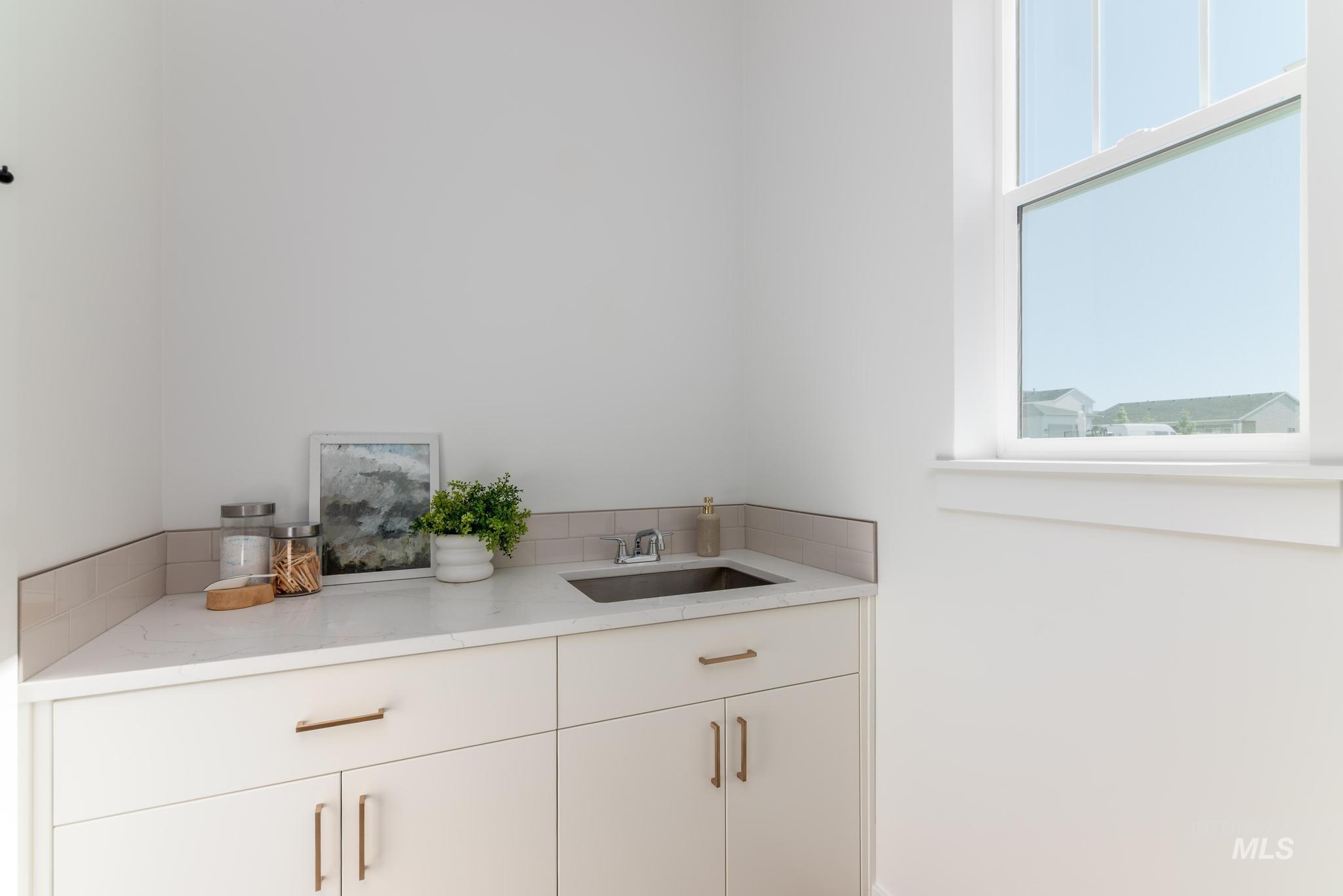 14703 Serenity Pt Street Caldwell, ID 83607 - Photo 24 of 45 Bright utility space featuring a single-pane window, white cabinetry with bronze hardware, a white countertop, and a stainless steel undermount sink