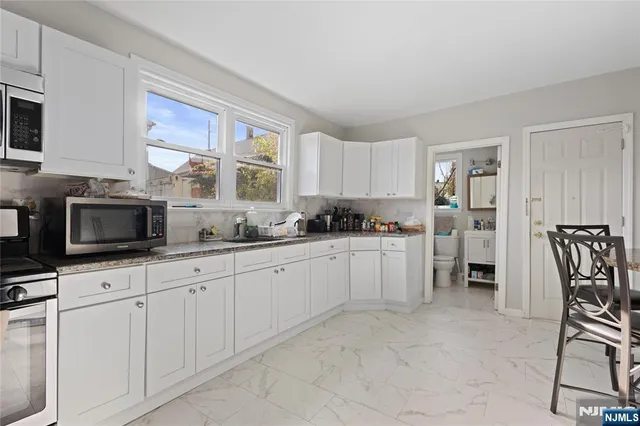 a kitchen with granite countertop white cabinets a window and stainless steel appliances