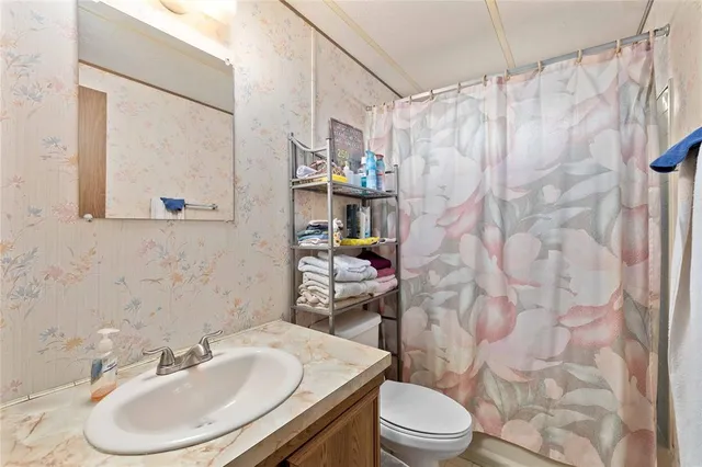 a bathroom with a granite countertop sink a toilet a large mirror a vanity and shower