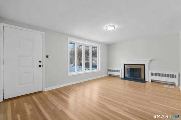 a view of an empty room with wooden floor fireplace and a window