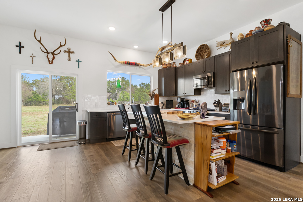 175 Pine Tree Road Medina, TX 78055 - Photo 16 of 34 a kitchen with stainless steel appliances granite countertop a refrigerator a sink dishwasher a dining table and chairs with wooden floor