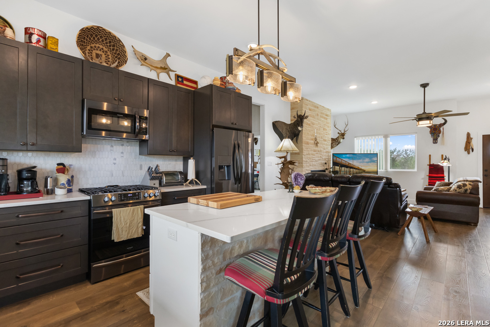 175 Pine Tree Road Medina, TX 78055 - Photo 18 of 34 a kitchen with stainless steel appliances granite countertop a stove a refrigerator a kitchen island a dining table and chairs with wooden floor