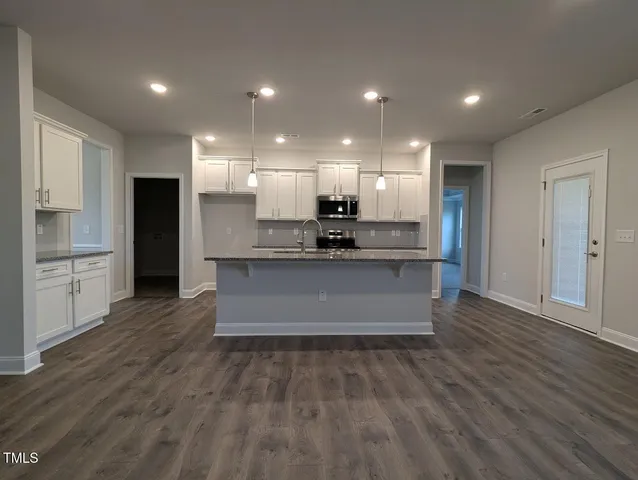 a large kitchen with kitchen island a stove a refrigerator a sink and white cabinets with wooden floor