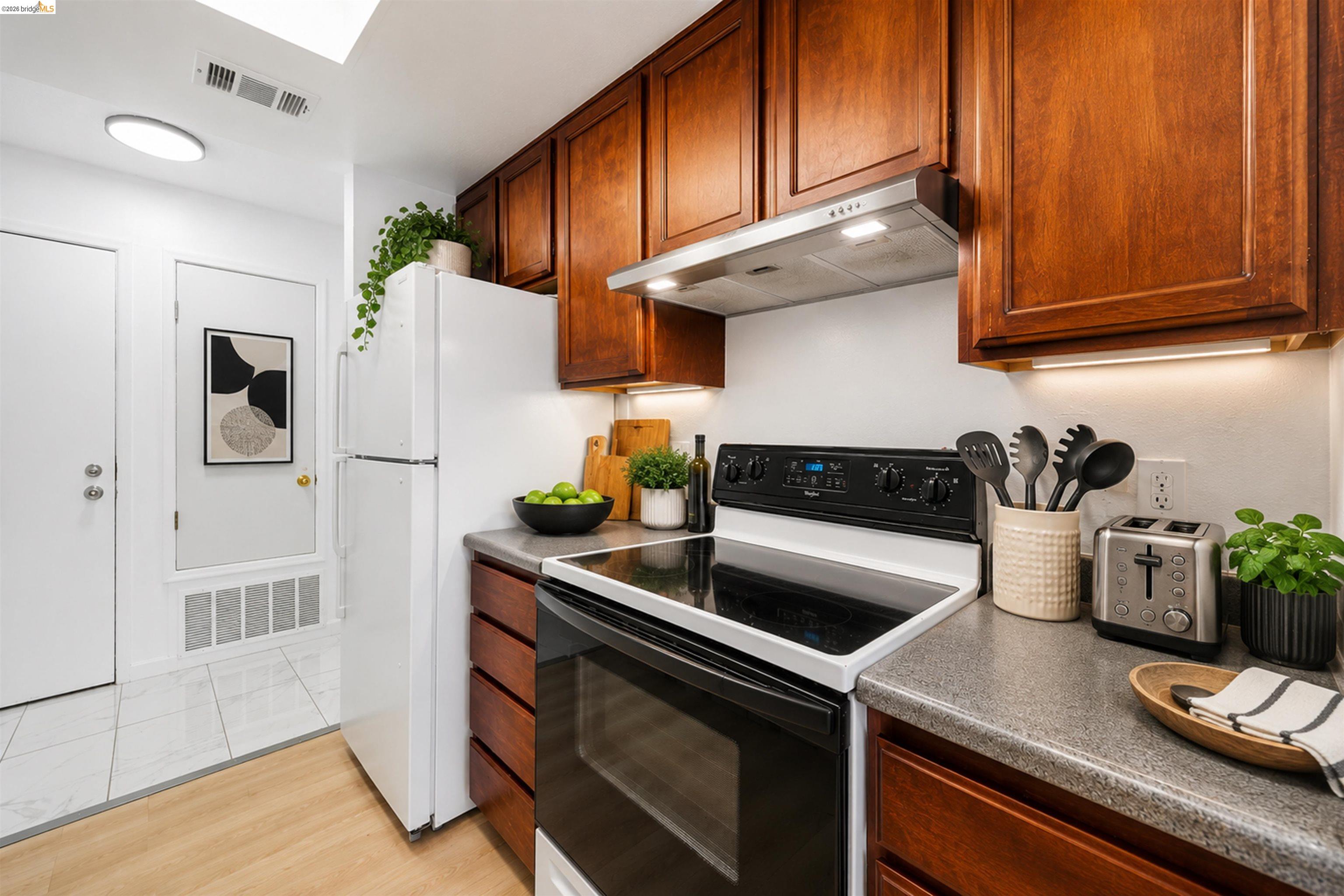 4186 San Pablo Dam Road, Unit A El Sobrante, CA 94803 - Photo 20 of 34 Well-appointed kitchen featuring wood-finish cabinetry, solid surface countertops, a white top-freezer refrigerator, and a black electric range with a stainless steel vent hood