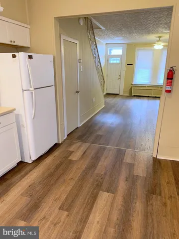 a view of a refrigerator in kitchen and an empty room with wooden floor