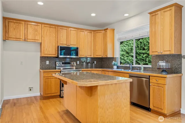 a kitchen with stainless steel appliances granite countertop a sink a stove a refrigerator with grey cabinets and wooden floor