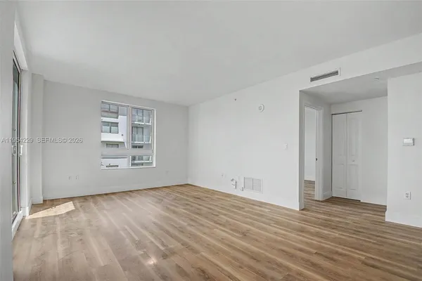 a view of an empty room with wooden floor and a window