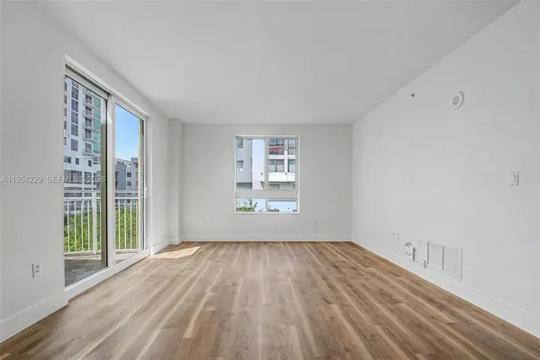 a view of an empty room with wooden floor and a window