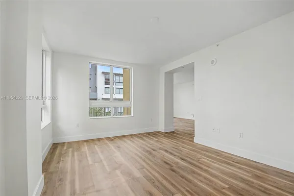 a view of an empty room with wooden floor and a window