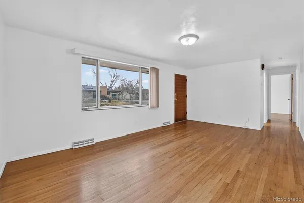 a view of an empty room with wooden floor and a window