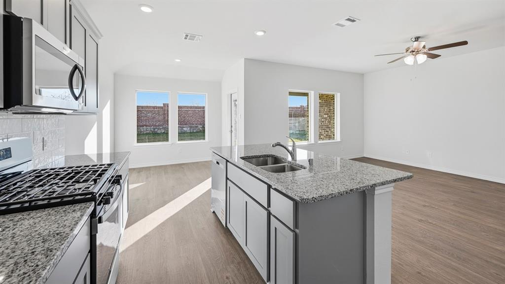419 Epiphany Lane Lavon, TX 75166 - Photo 6 of 31 Open-concept kitchen and living area featuring a central island with a double basin sink, granite countertops, stainless steel appliances, wood-finish flooring, and recessed lighting