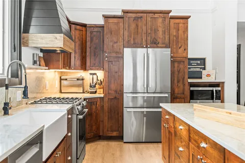 a kitchen with stainless steel appliances granite countertop a refrigerator a stove and a sink with wooden cabinets