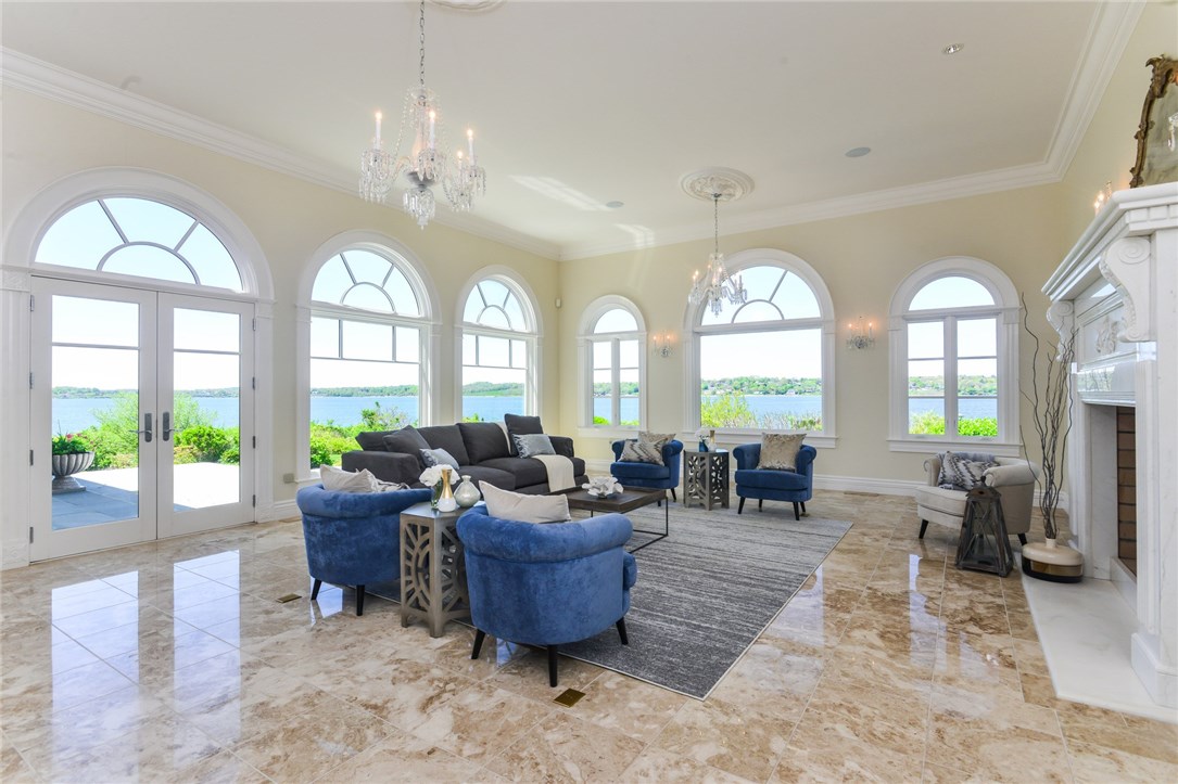 137 High Hill Road Tiverton, RI 02878 - Photo 8 of 39 The spacious living room with custom carved marble fireplace and floors is surrounded by windows overlooking the sparkling Sakonnet Passage. Custom chandeliers and sconces were created just for this space and throughout the home. UV protected windows provide views without glare or sun-fading.