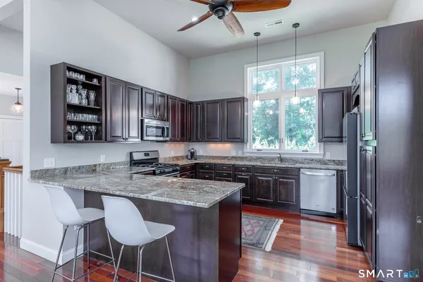 a kitchen with stainless steel appliances granite countertop a stove a sink dishwasher a refrigerator and a dining table with wooden floor