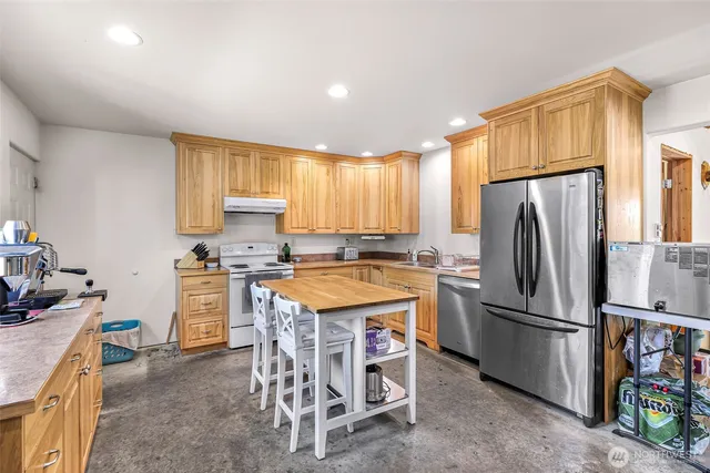 a kitchen with stainless steel appliances a refrigerator a sink a stove top oven a dining table and chairs