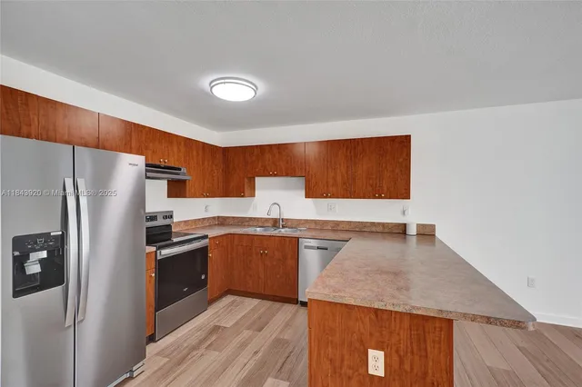 a kitchen with stainless steel appliances granite countertop a refrigerator a sink dishwasher and wooden cabinets with wooden floor