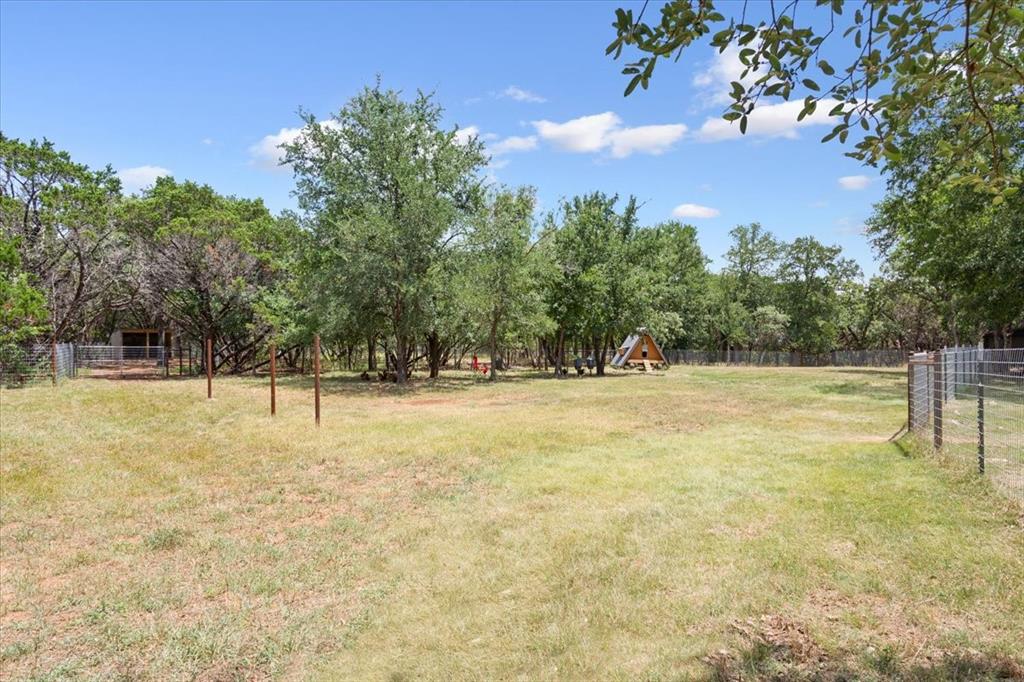 15988 Wortham Bend Road China Spring, TX 76633 - Photo 40 of 40 Expansive grassy area featuring mature trees, a partial fence line, and a small A-frame structure in the distance