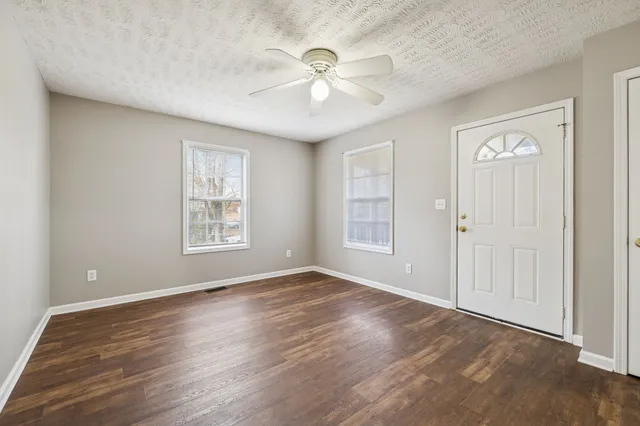 an empty room with wooden floor chandelier fan and windows