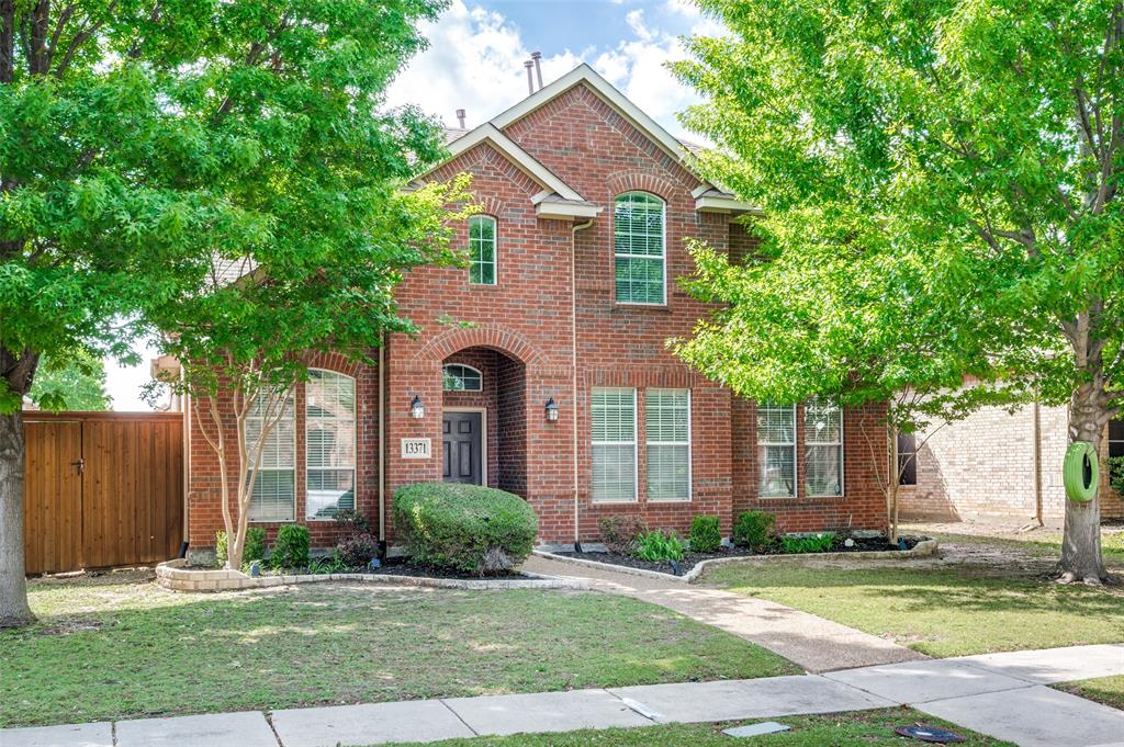 The property features a brick exterior, an arched entryway, and a well-maintained lawn with mature trees