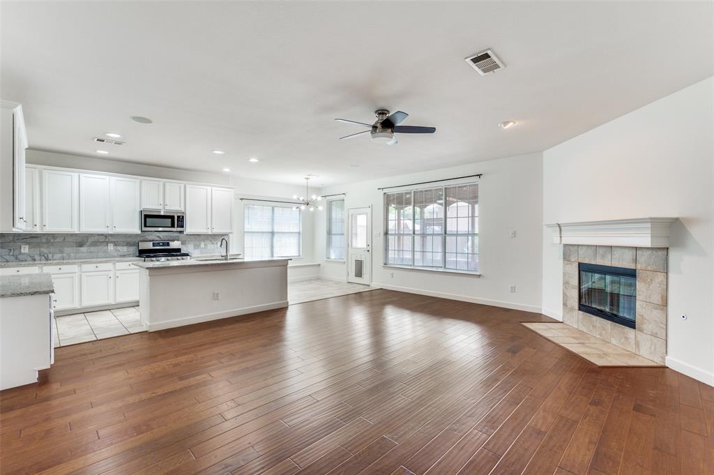 13371 Lime Ridge Drive Frisco, TX 75033 - Photo 8 of 25 Open concept living area featuring hardwood floors, a kitchen with white cabinetry and stainless steel appliances, and a fireplace with a tiled surround