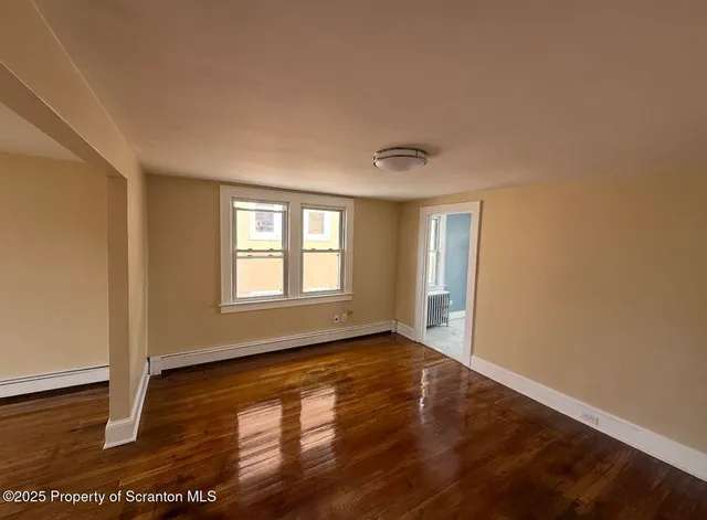 a view of an empty room with wooden floor and a window