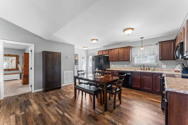 a kitchen with stainless steel appliances granite countertop a refrigerator a stove a sink a dining table and chairs with wooden floor